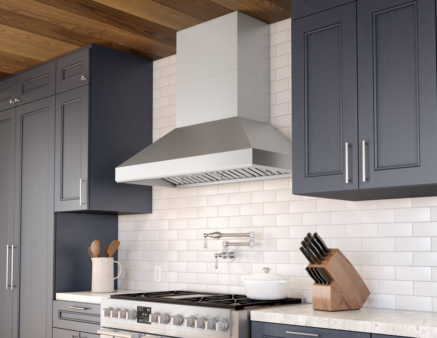 Modern stainless steel chimney range hood above gas cooktop in kitchen with dark blue cabinetry and wood ceiling paneling