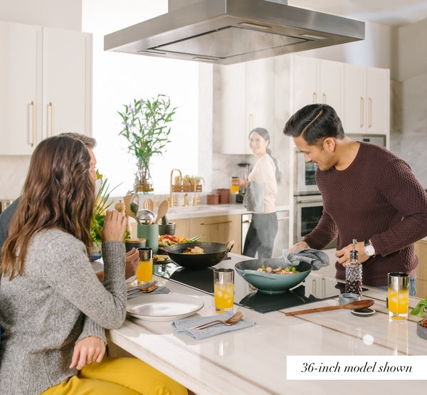 Modern kitchen scene with people cooking and dining under a stainless steel island range hood from Thermador collection