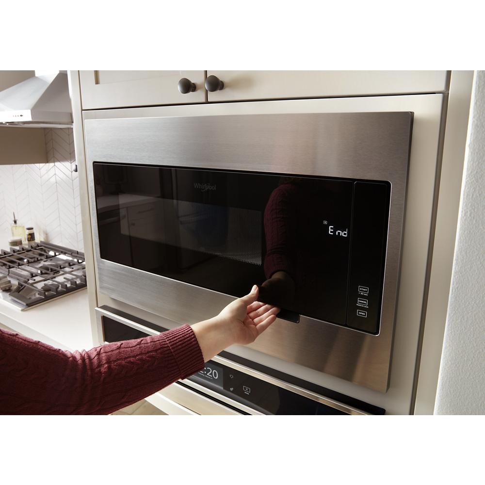 Hand reaching to open stainless steel built-in microwave with slim trim kit in modern kitchen setting