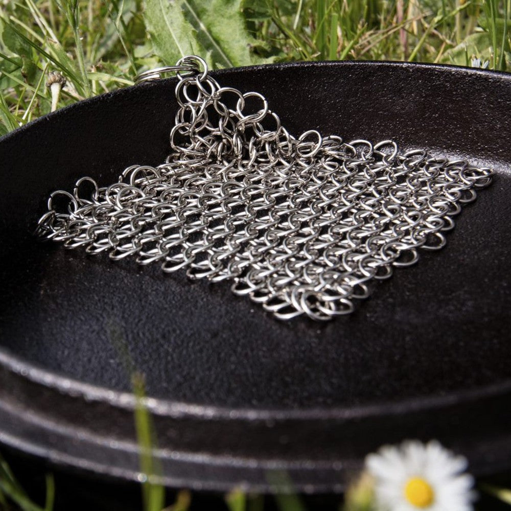 Stainless steel chainmail scrubber resting inside cast iron skillet on grass for kitchenware and home improvement tools