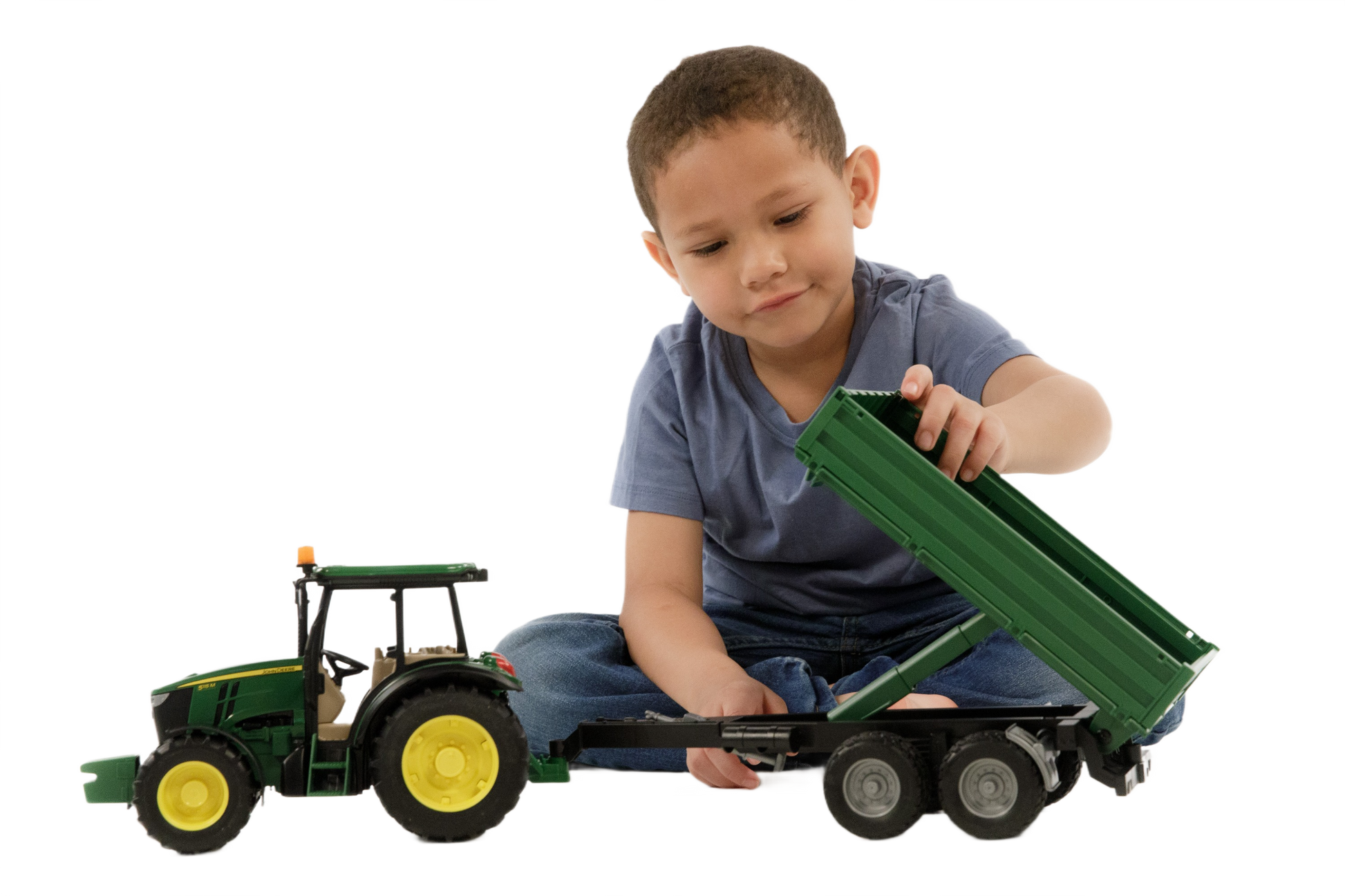 Young child playing with green Bruder John Deere 5115M toy tractor and attached trailer with raised bed