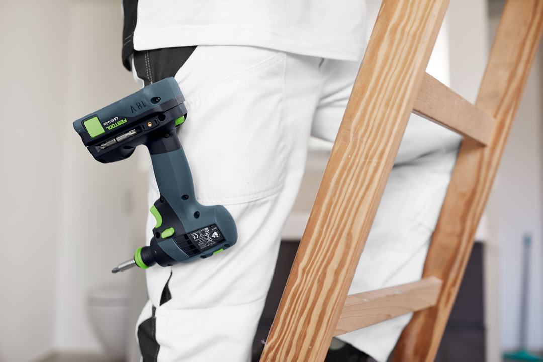 Festool cordless drill clipped to belt on person wearing white pants beside wooden ladder for home improvement