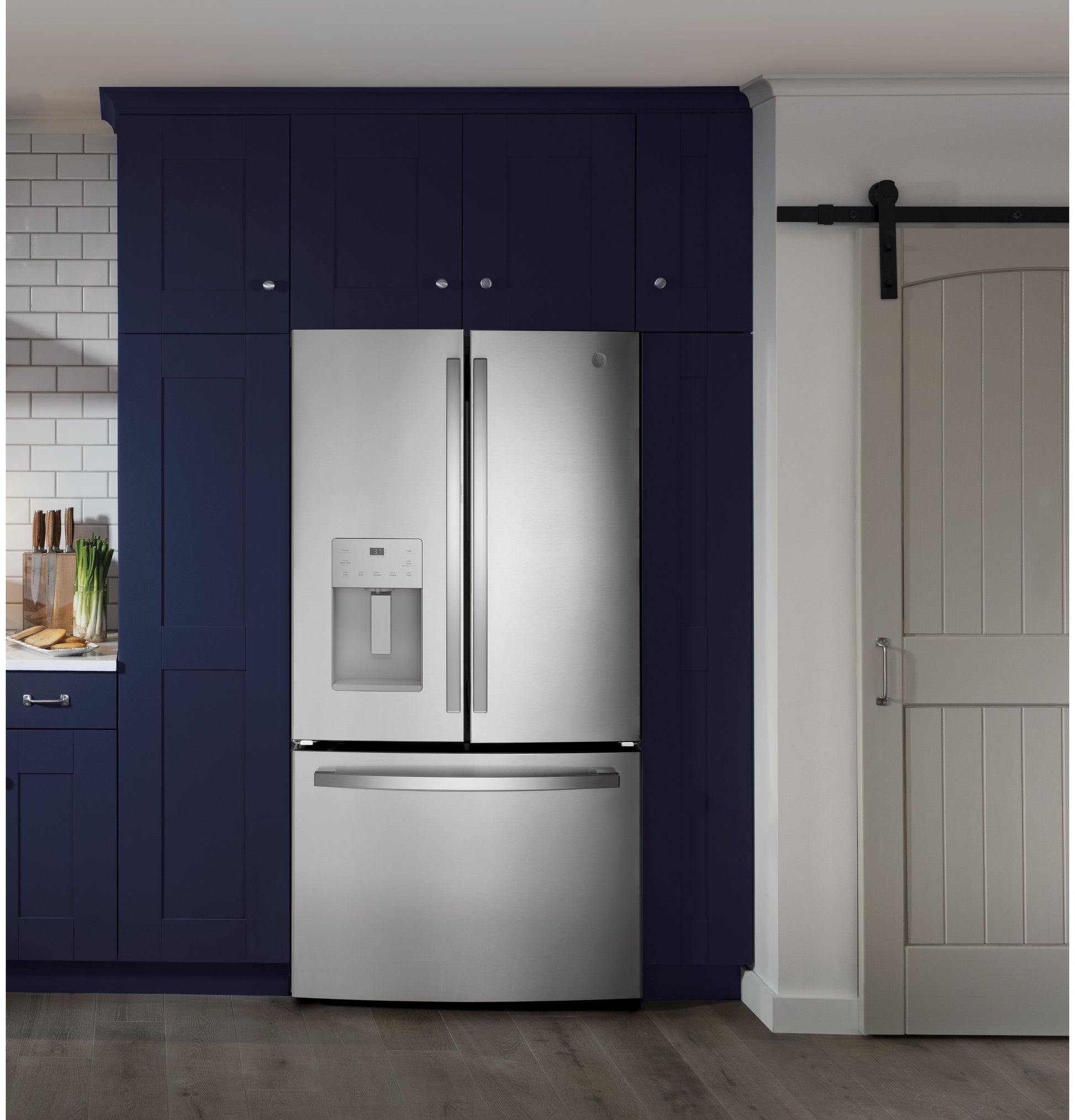 Fingerprint resistant stainless steel French-door refrigerator with bottom freezer integrated into navy blue kitchen cabinetry in appliances collection