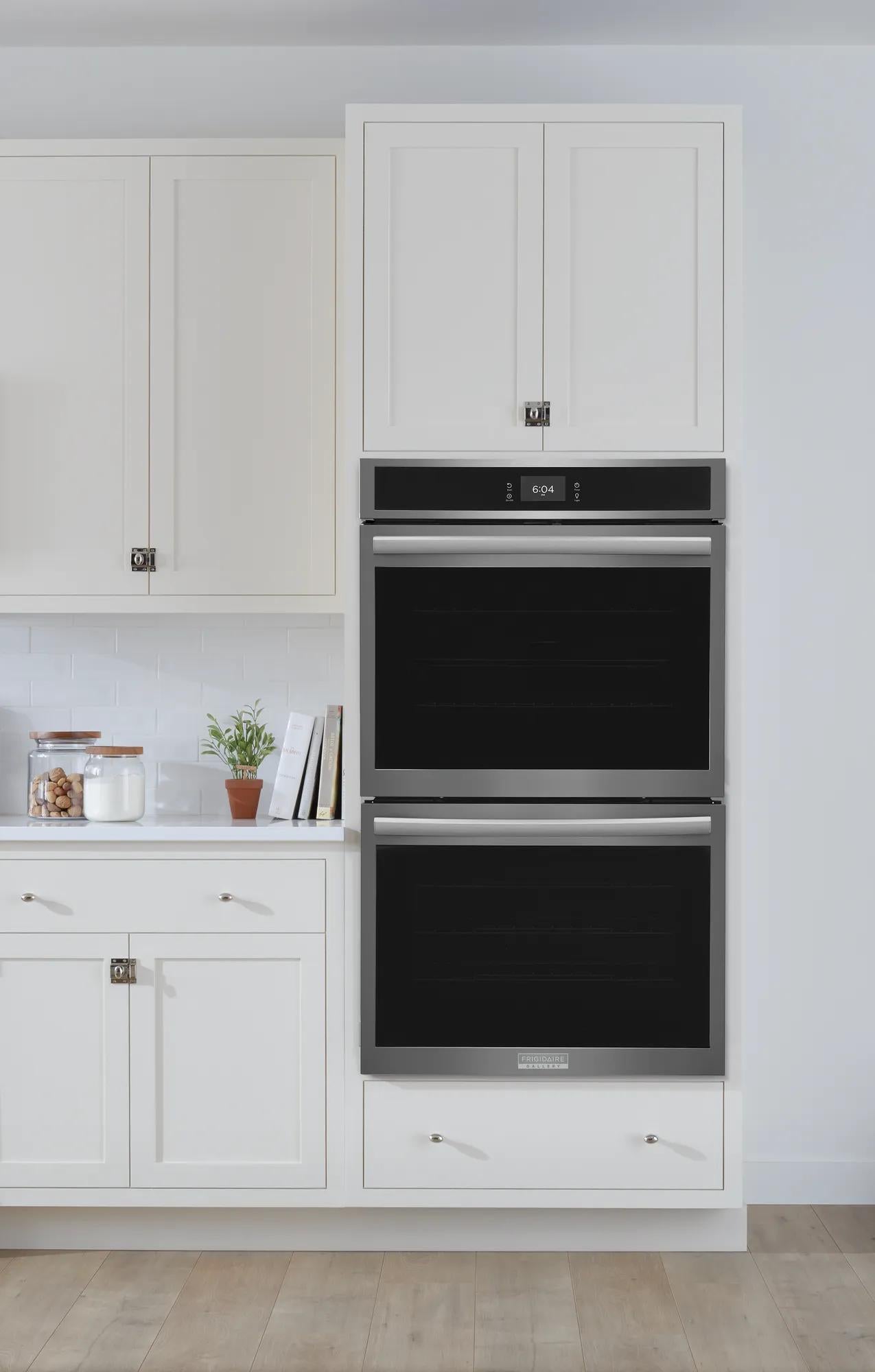 Built-in double electric wall oven with stainless steel trim integrated into white kitchen cabinetry and hardwood flooring.