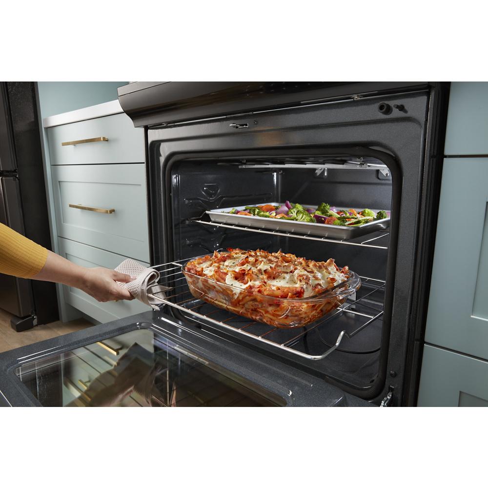 Person removing a baked pasta dish from a black electric range oven with roasted vegetables on second rack inside
