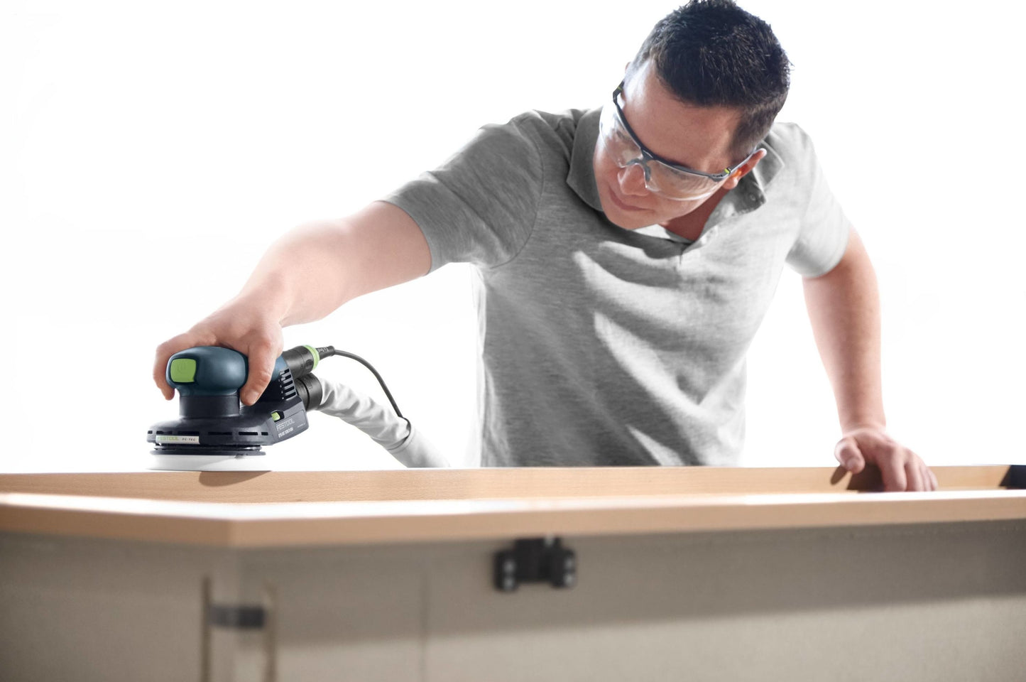 Man using a random orbit sander on wood surface wearing safety glasses in a woodworking tools setting