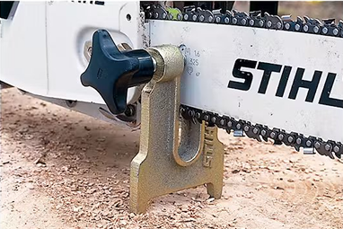 Metal tool accessory holding a chainsaw guide bar steady on wood for chain sharpening in power tool accessories.