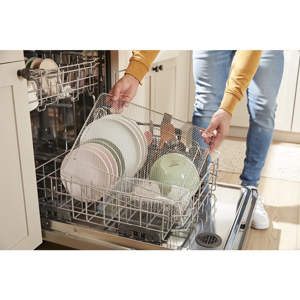 Person loading a mesh basket with plates and bowls into a dishwasher in a modern kitchen setting