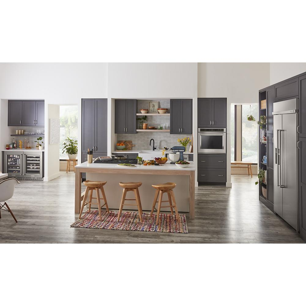 Modern kitchen featuring dark gray cabinetry, central island with wooden stools, and 24" undercounter refrigerator with glass door.