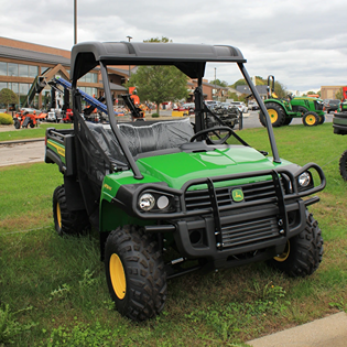 Green utility vehicle with sturdy frame and off-road tires displayed outdoors on grass near other equipment