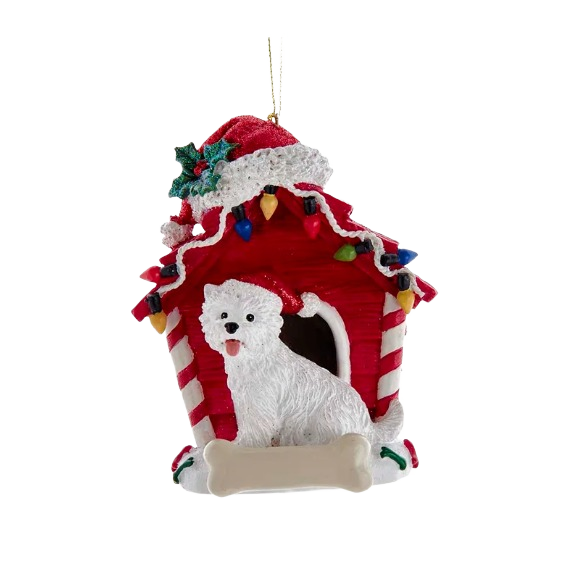 White West Highland Terrier figurine sitting in front of a red doghouse ornament with Christmas lights and holiday decor