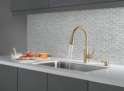 Champagne bronze kitchen faucet with single handle and soap dispenser installed over stainless steel sink in modern kitchen setting