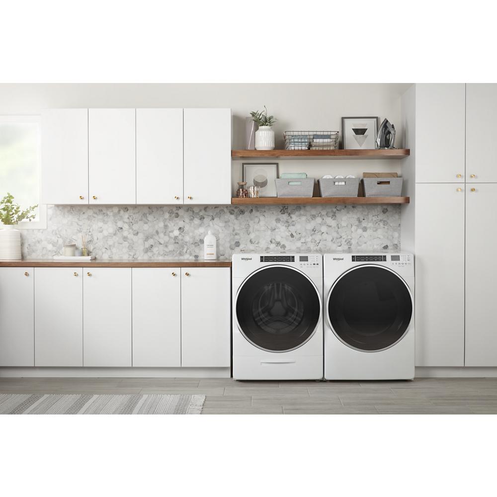 White front load washer and dryer pair with digital controls in a modern laundry room featuring wood shelves and white cabinetry
