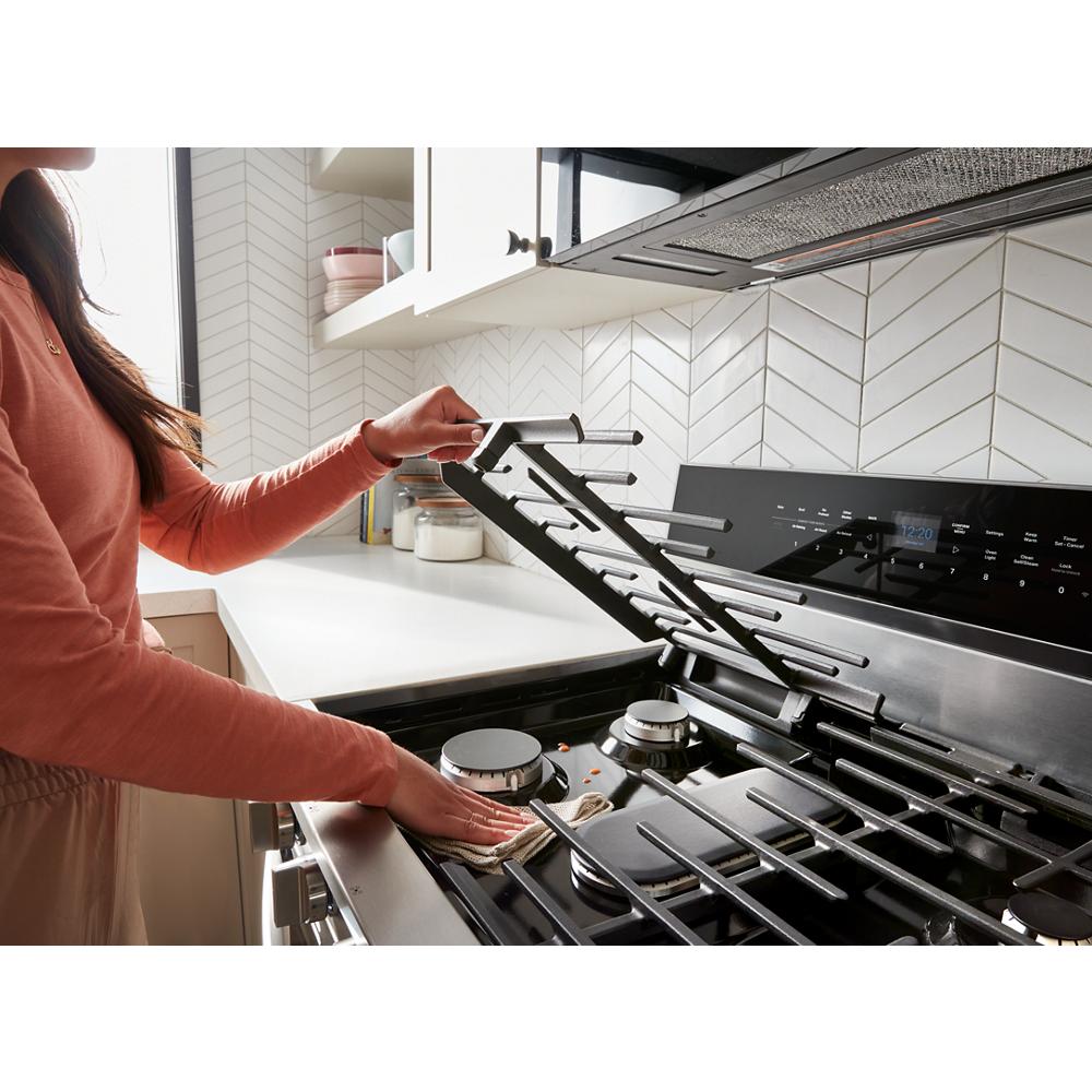 Person lifting dishwasher-safe hinged cast grate on stainless steel gas range in modern kitchen appliances collection