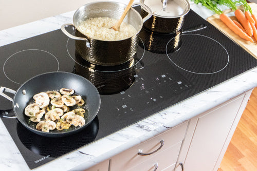 European black mirror induction cooktop with five cooking zones preparing rice and sautéed mushrooms in a home kitchen setting