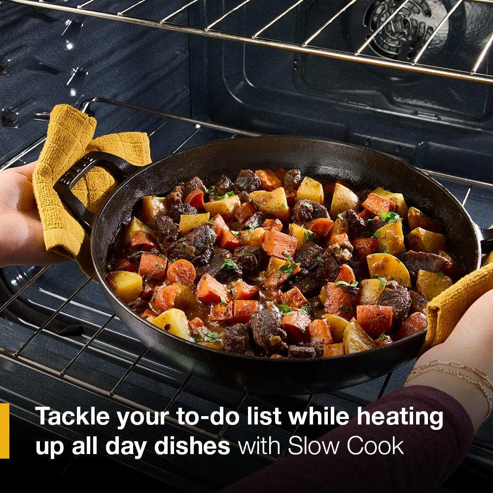 Hands removing cast iron skillet with roasted vegetables and meat from oven in kitchen appliance setting