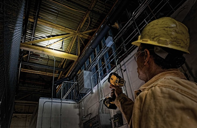Worker wearing hard hat using a portable DEWALT spotlight to illuminate an industrial workspace at night