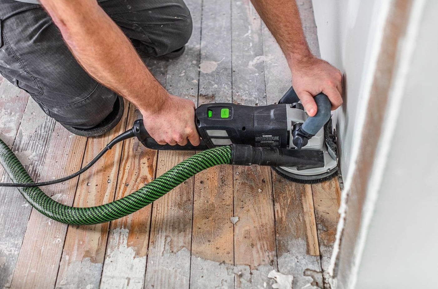 Person using a Festool diamond grinder to smooth a wood floor near a wall in a home improvement setting