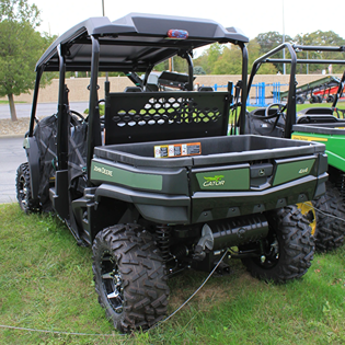 Rear view of a green John Deere off-road utility vehicle with rugged tires and cargo bed on grassy terrain
