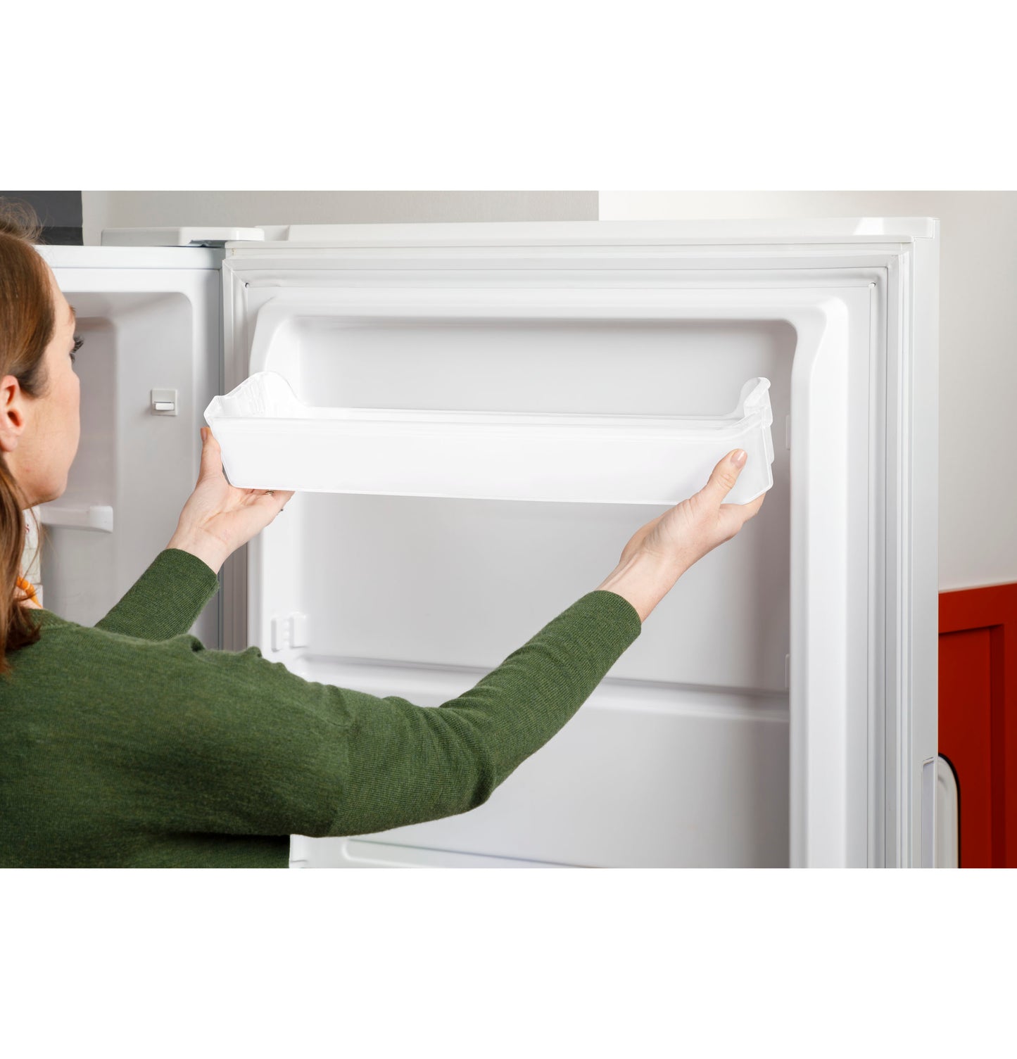 Person installing a removable door bin inside a white frost-free upright freezer in a kitchen setting