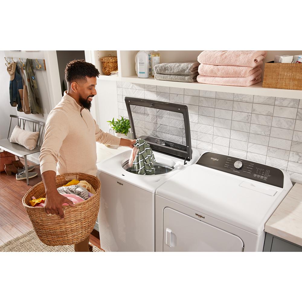 Man loading clothes into top load washer next to white gas dryer in bright laundry room with folded towels