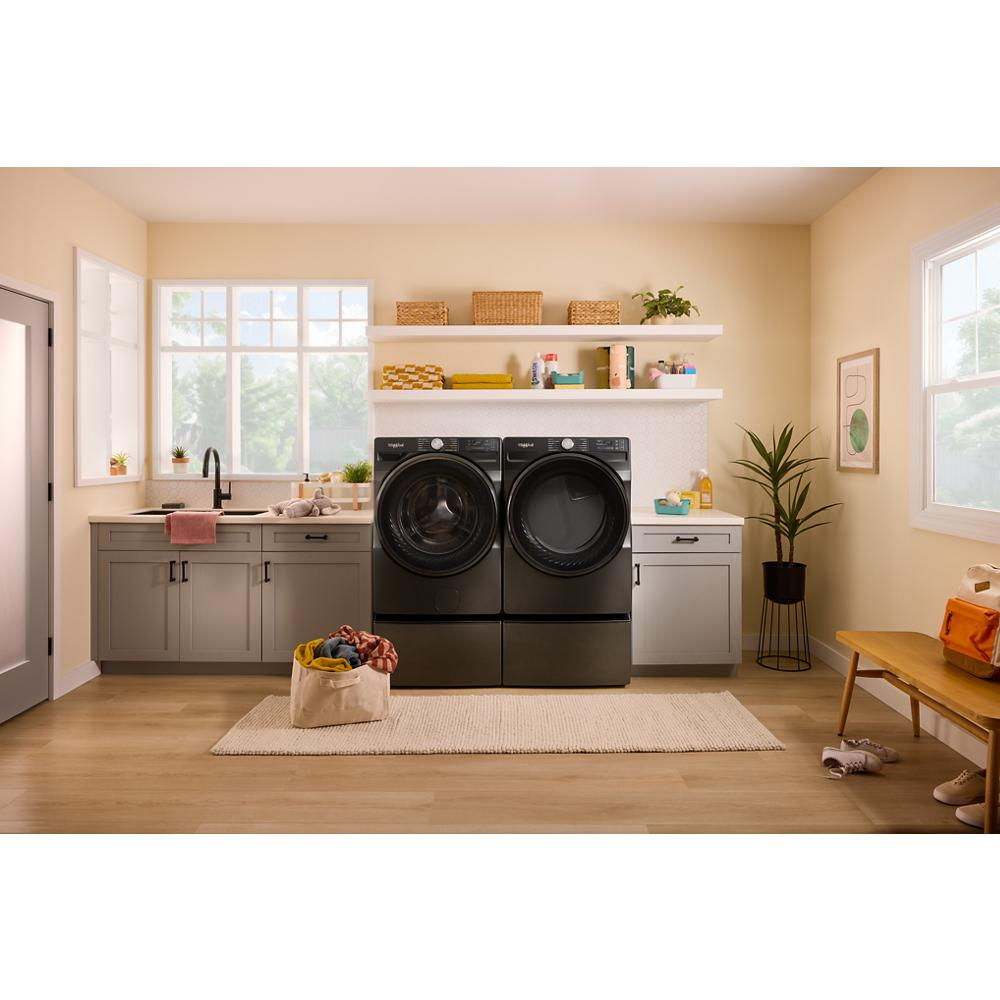 Black smart front load electric washer and dryer in a bright laundry room with gray cabinetry and wooden floorboards