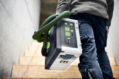Person carrying cordless HEPA dust extractor with green hose up stairs for dust collection in woodworking tools collection