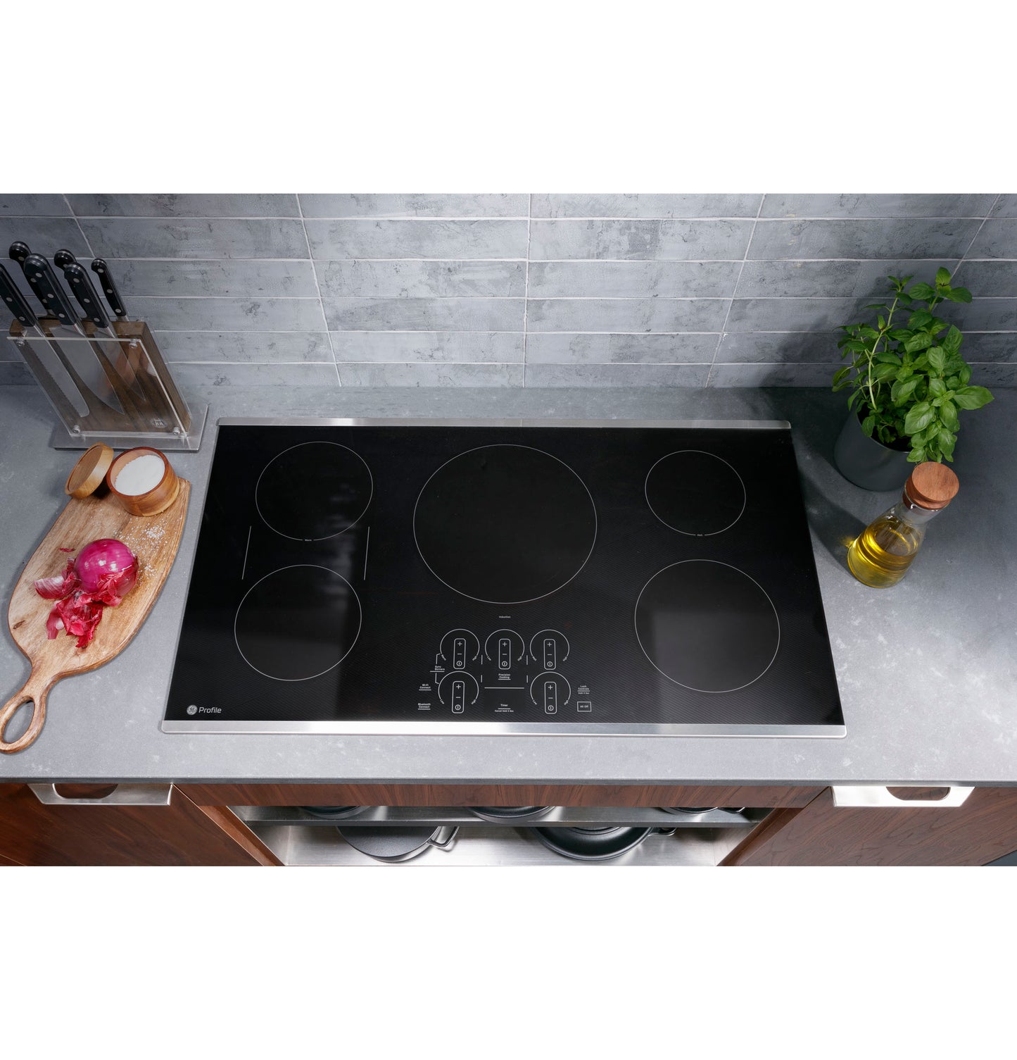 Black built-in induction cooktop with five touch control cooking zones set in modern kitchen countertop with herb plant and knife block