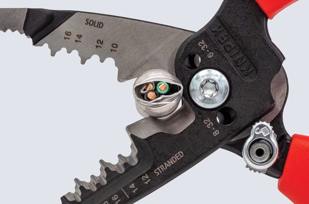 Close-up of forged wire strippers gripping a copper electrical cable with red handles for precise home improvement tasks