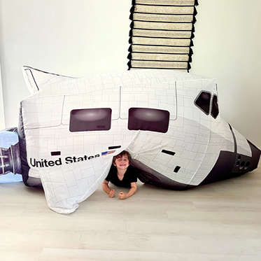 Child smiling and playing inside a white inflatable space shuttle play tent with black and gray details indoors