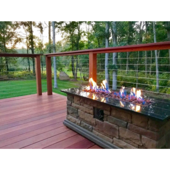 Outdoor deck with reddish wooden planks and cable rail assembly overlooking a green yard with a stone fire pit table