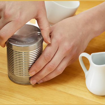 Hands using RSVP Vintage Punch N' Cover stainless steel tool sealing a canned food on wooden kitchen surface