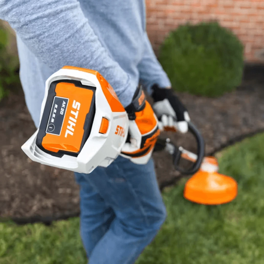 Close-up of orange and white rechargeable lithium-ion battery attached to outdoor handheld gardening tool
