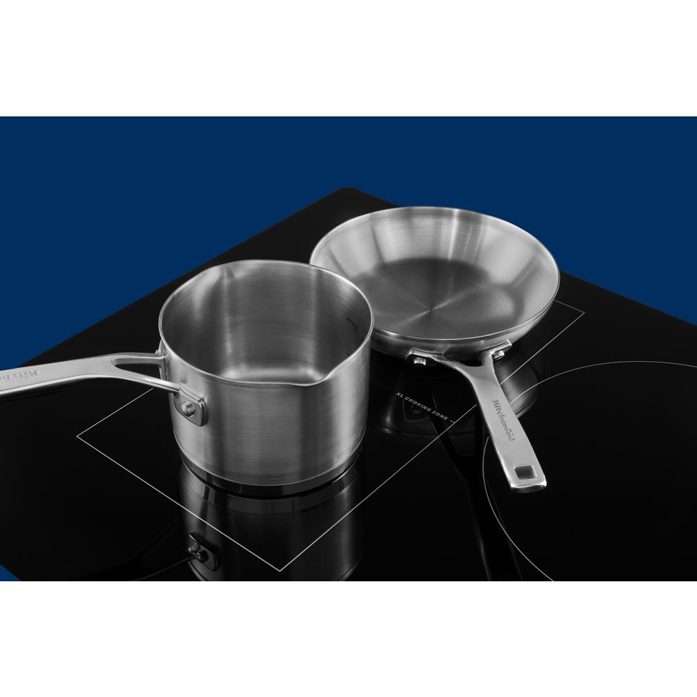 Black induction cooktop with two stainless steel pans on outlined cooking zones in kitchen and cookware collection
