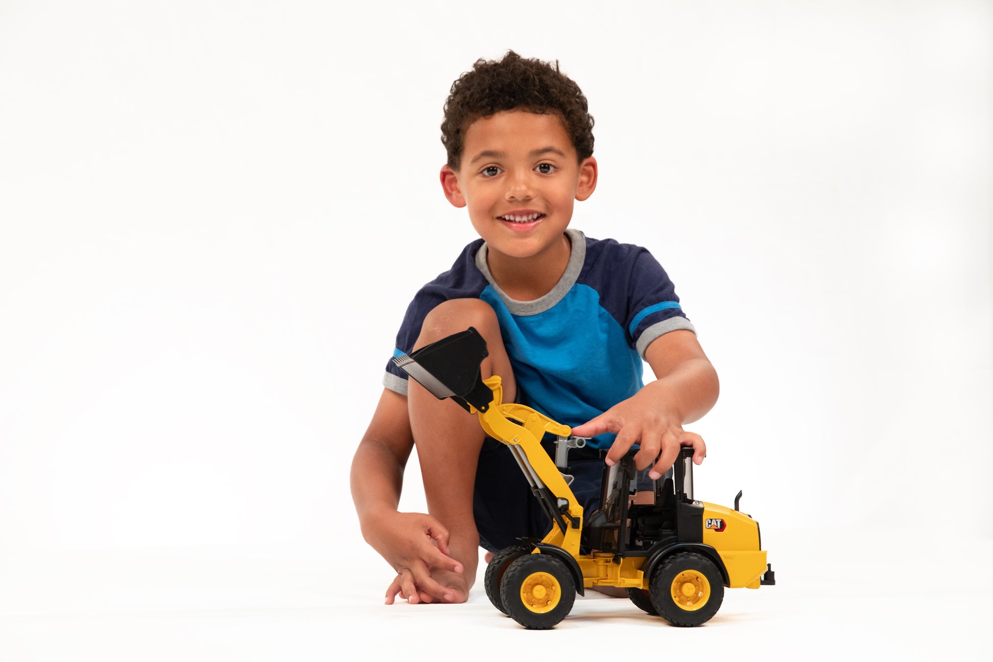 Young boy playing with yellow Bruder CAT wheel loader toy promoting tools and home improvement interests