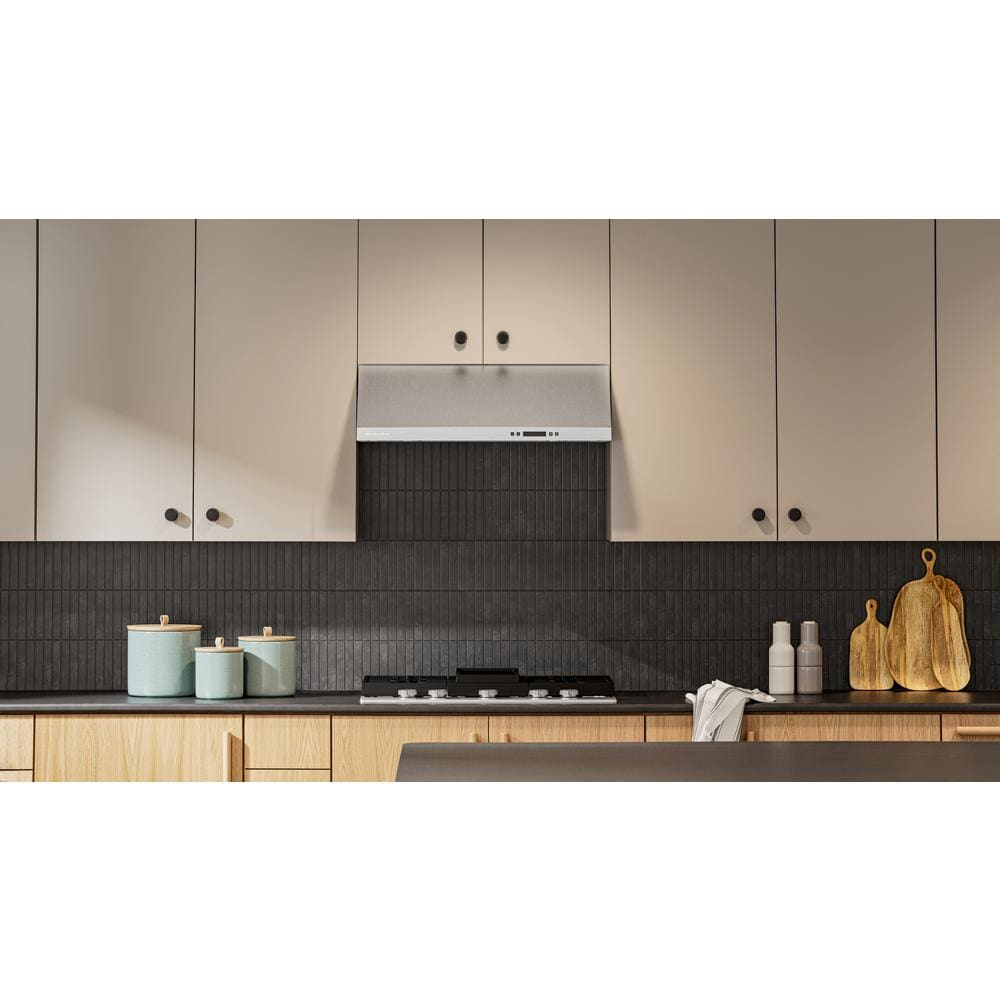 Under-cabinet ventilation system with stainless steel finish above gas cooktop in modern kitchen with wood and dark tile accents