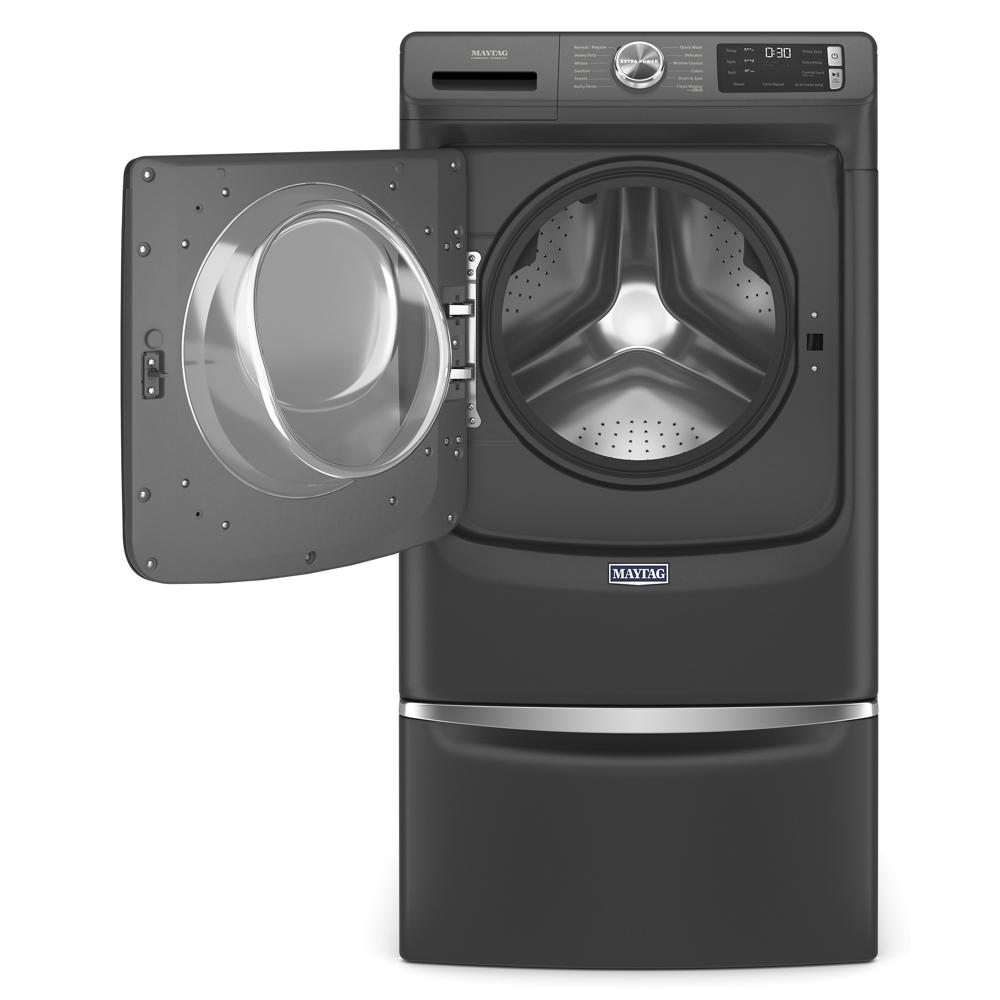 Dark gray front load washer with digital controls and open door, elevated on matching storage pedestal for laundry accessories