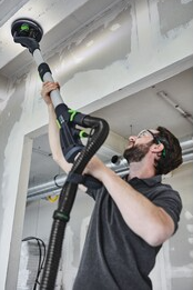 Man using Festool sanding tool with hose clip attachment for ceiling sanding in a home improvement setting