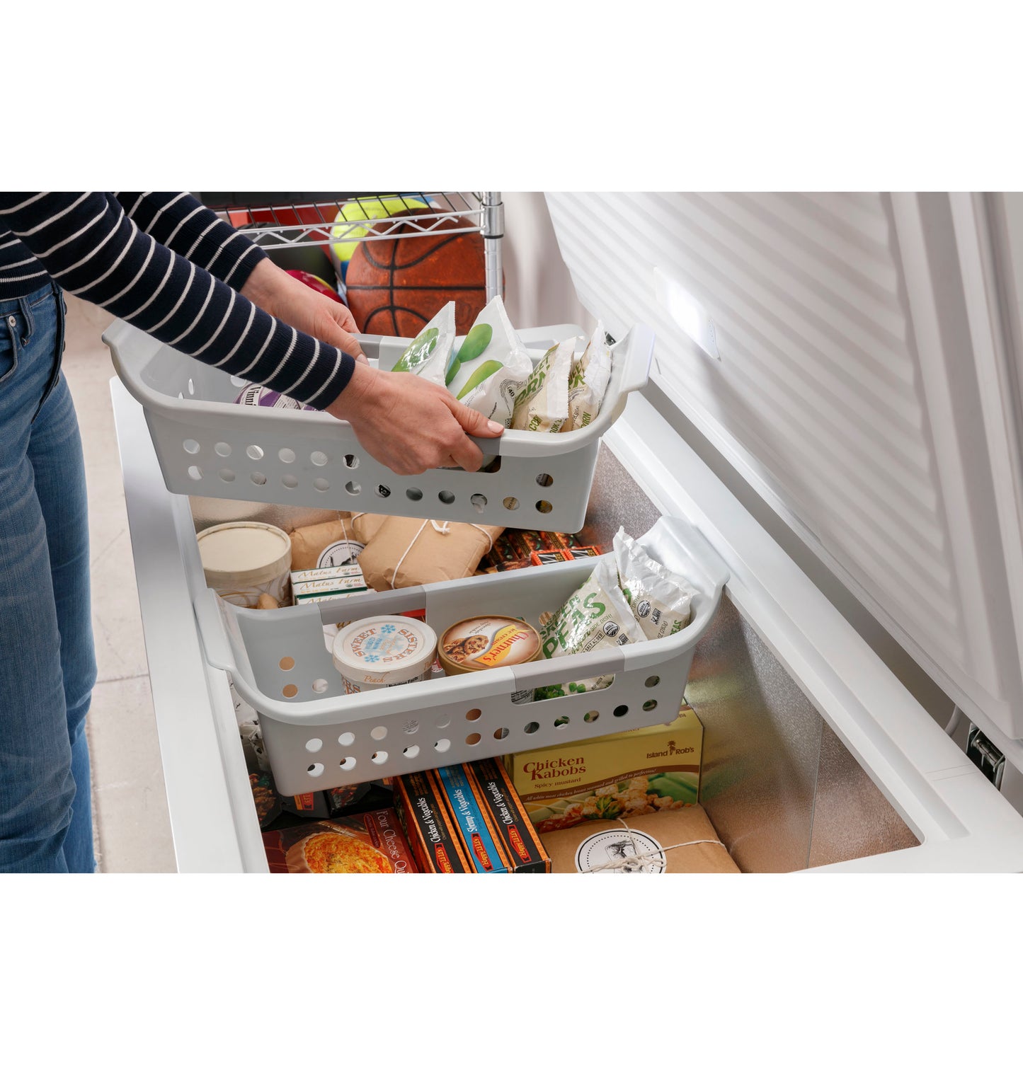 Person organizing frozen groceries in removable bins inside a white manual defrost chest freezer for kitchen storage