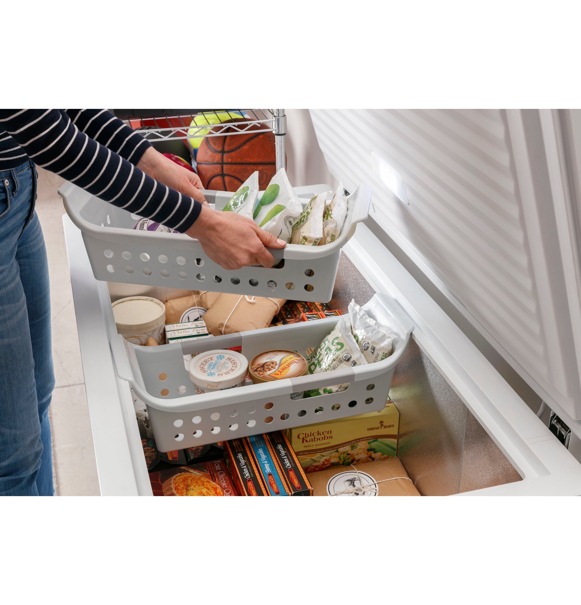 Person organizing frozen groceries in removable bins inside a white manual defrost chest freezer for kitchen storage