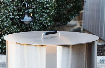 Round stainless steel fire pit lid with black grip handle for outdoor tools and home improvement use