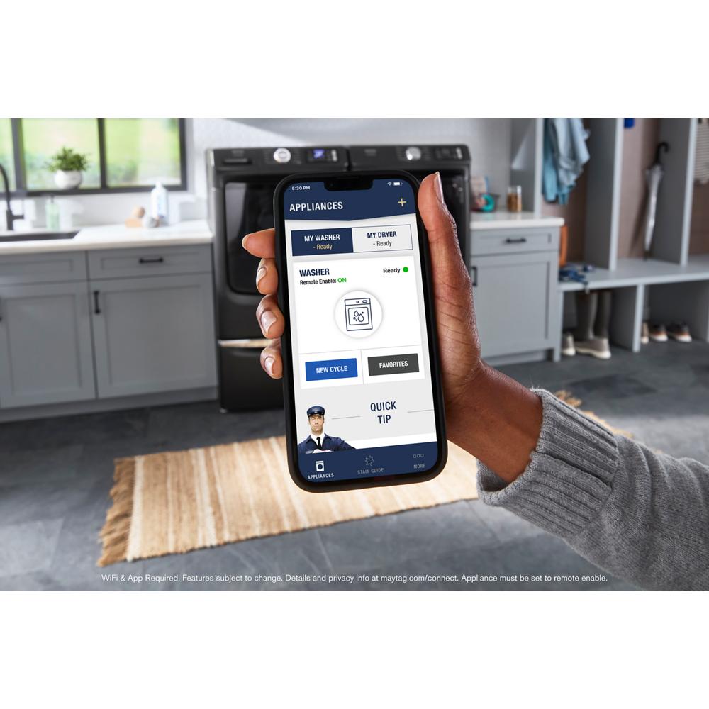 Hand holding smartphone showing appliance app with washer and dryer status in bright modern laundry room