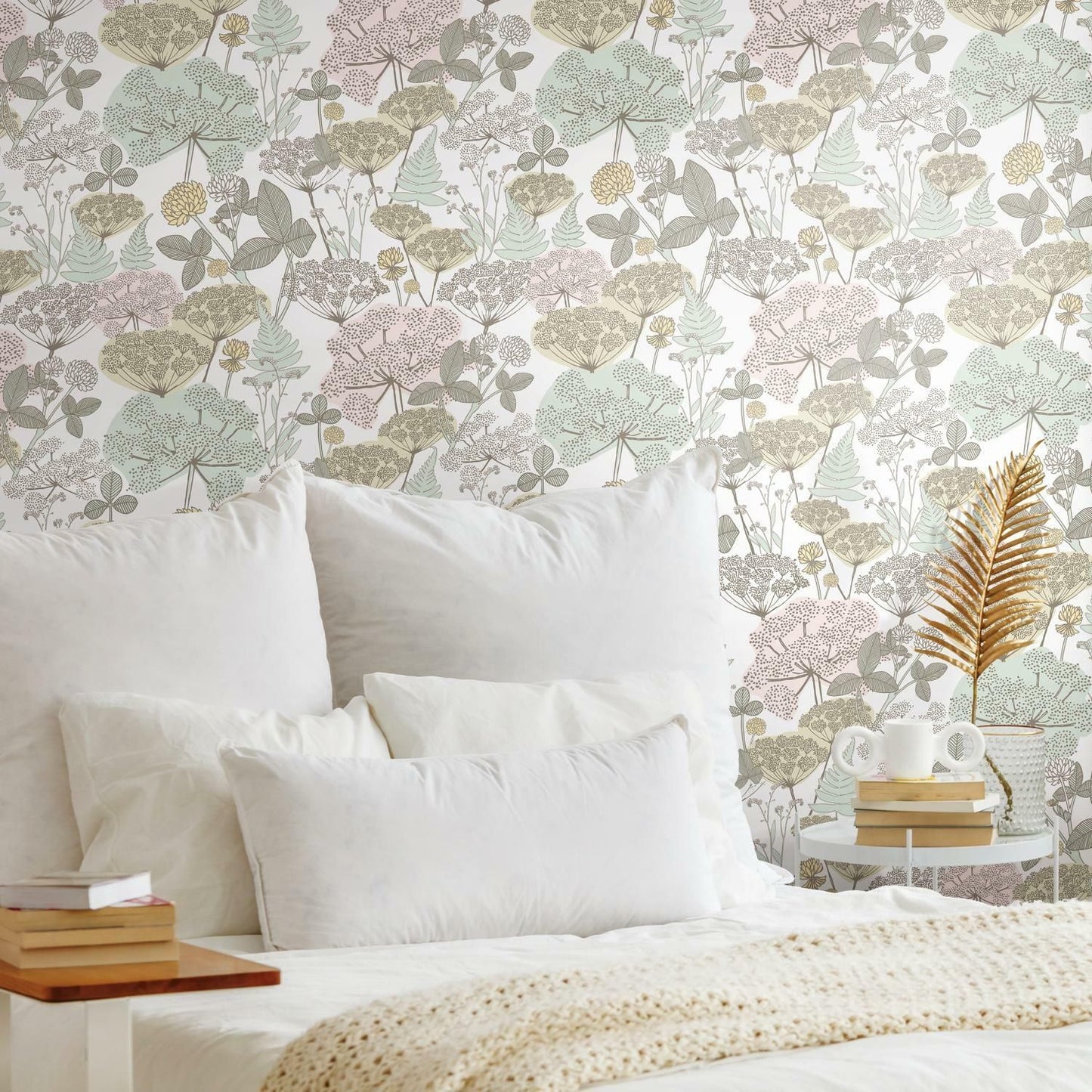Peel and stick wallpaper with soft pink and green floral pattern behind a bed with white pillows and cozy blanket