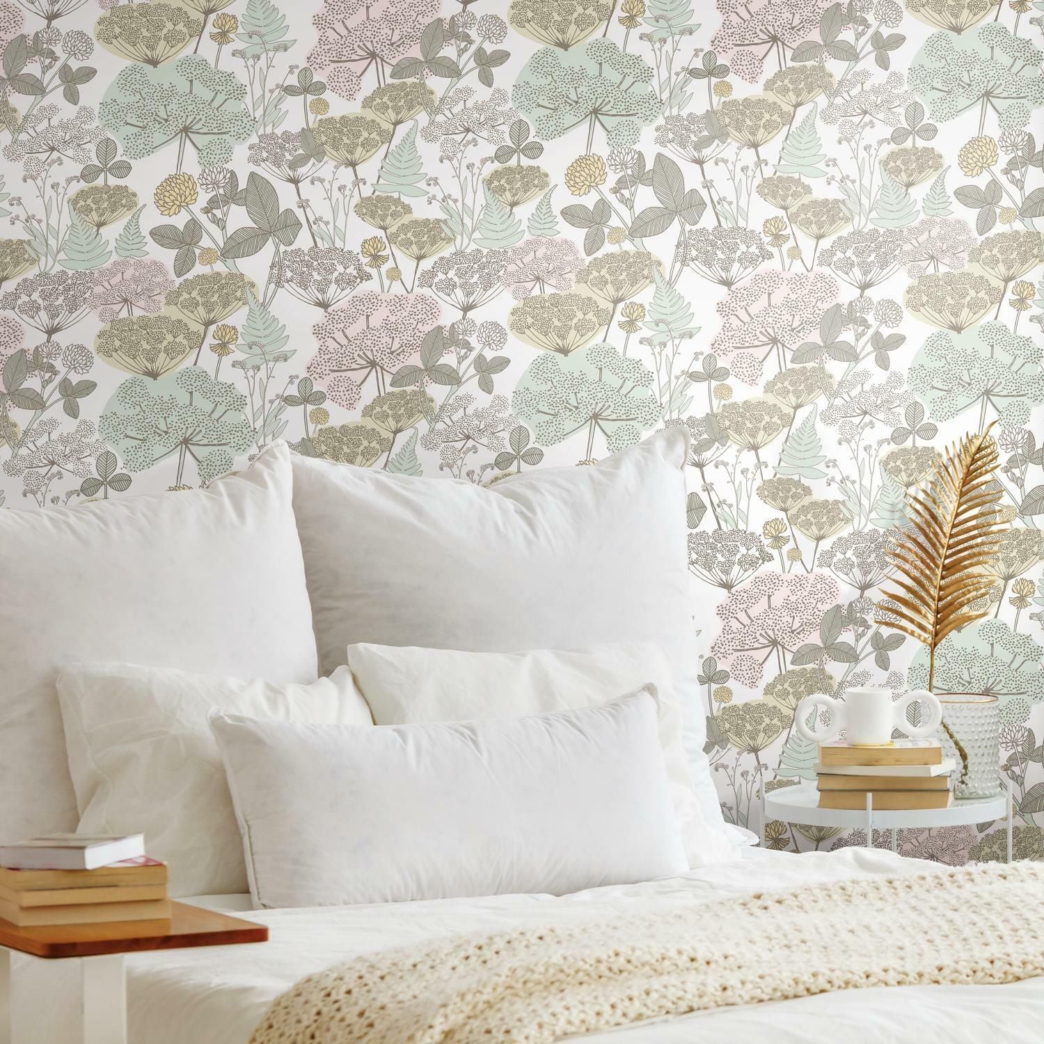 Peel and stick wallpaper with soft pink and green floral pattern behind a bed with white pillows and cozy blanket