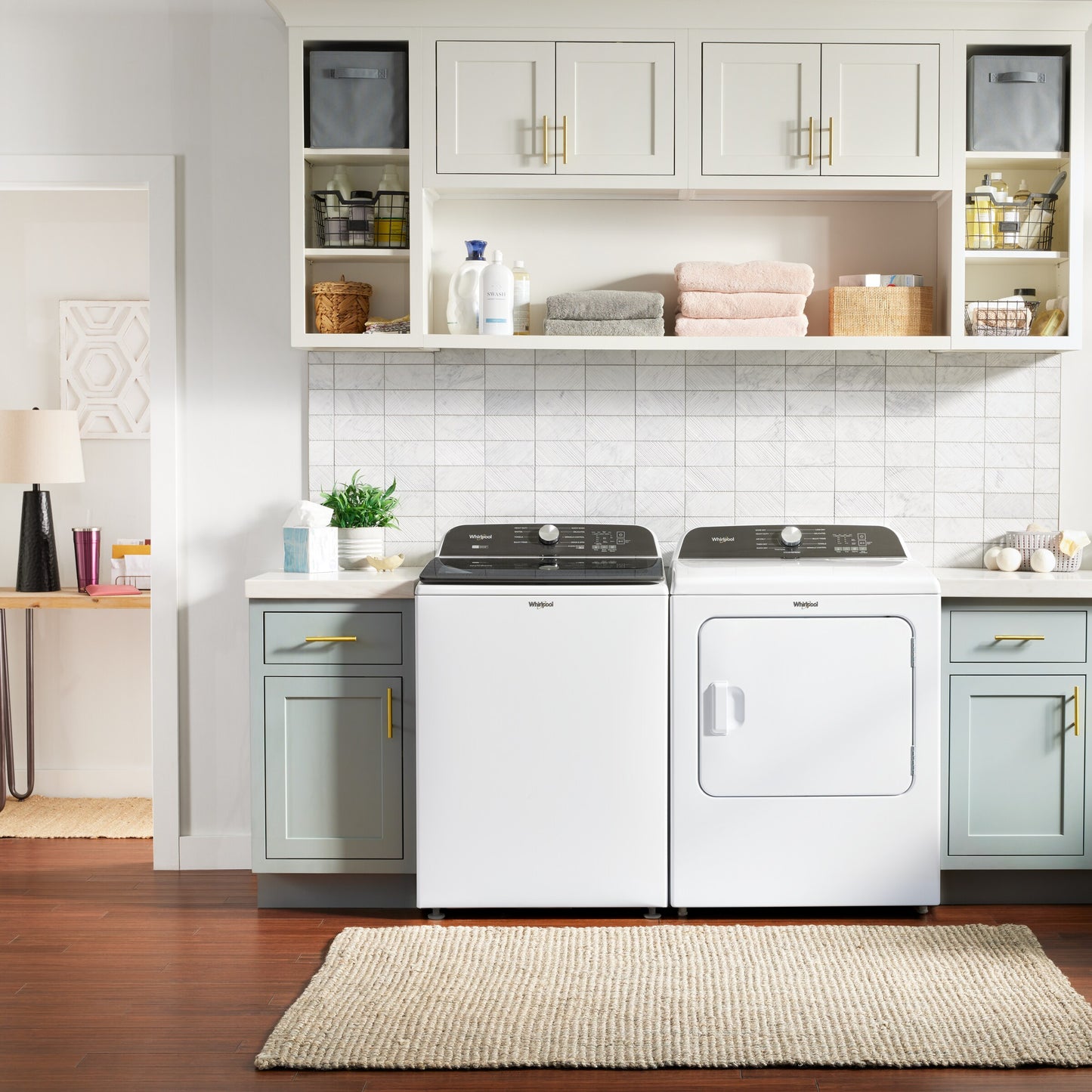 Modern laundry room with white top load gas dryer and matching washer, gray cabinets, and built-in shelving with decor