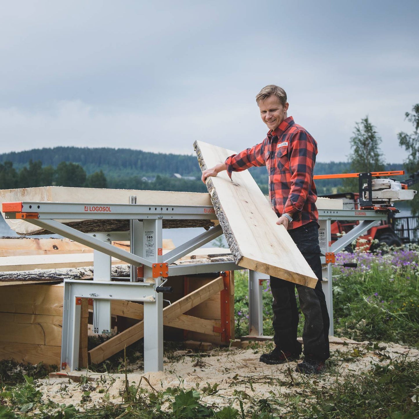 Man placing freshly milled wooden plank onto a portable chain sawmill outdoors with a forest backdrop