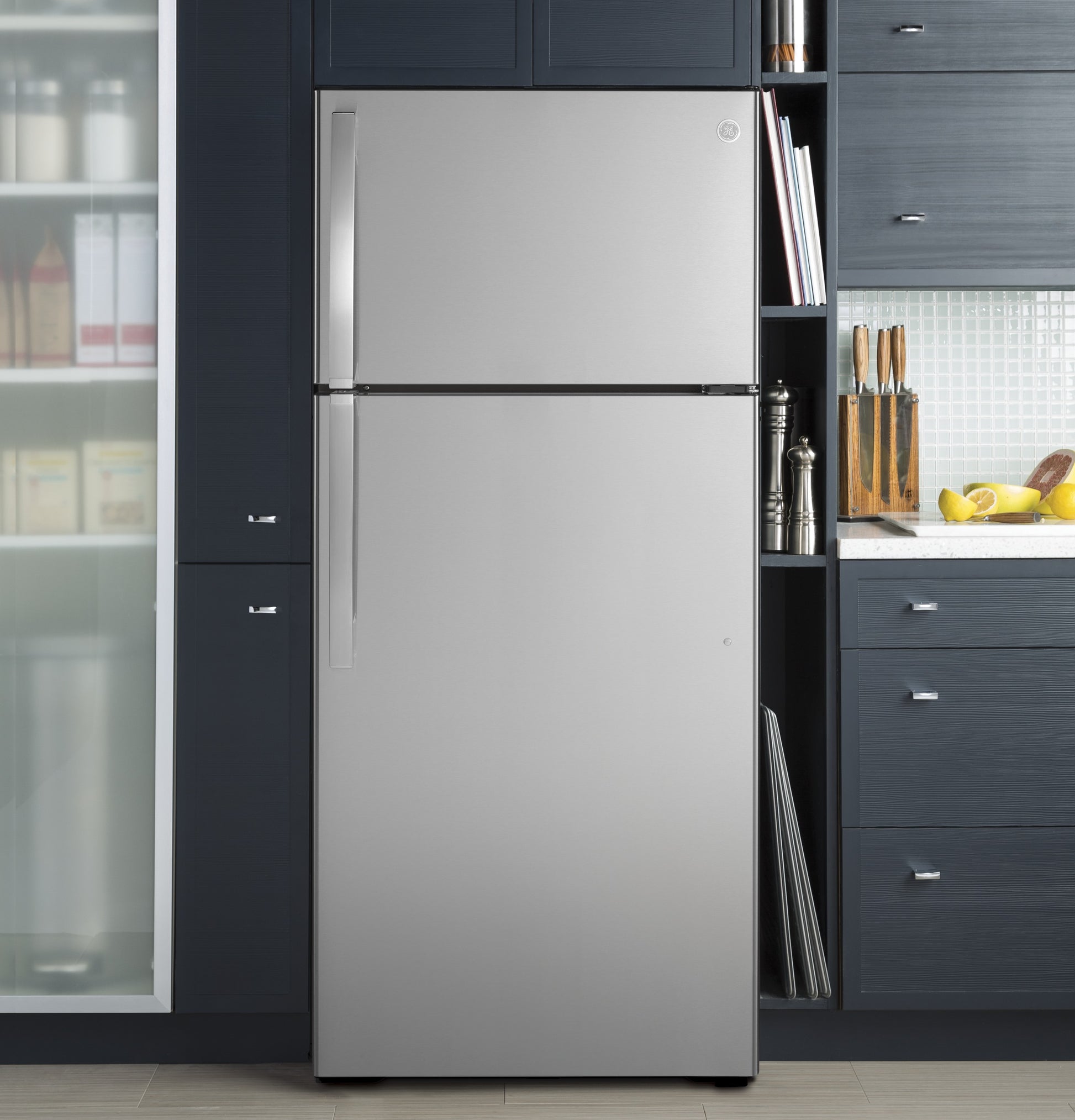Stainless steel top-freezer refrigerator integrated into dark blue kitchen cabinetry with countertop and cutting board nearby