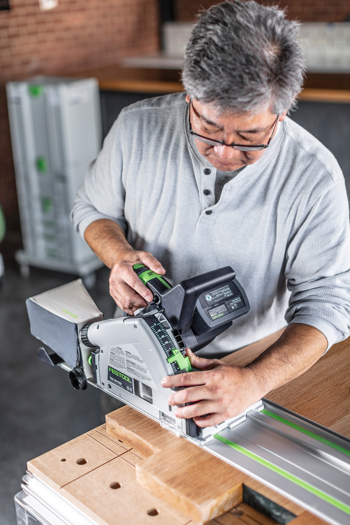 Man adjusting cordless Festool track saw on 55-inch guide rail cutting wood in workshop for home improvement task