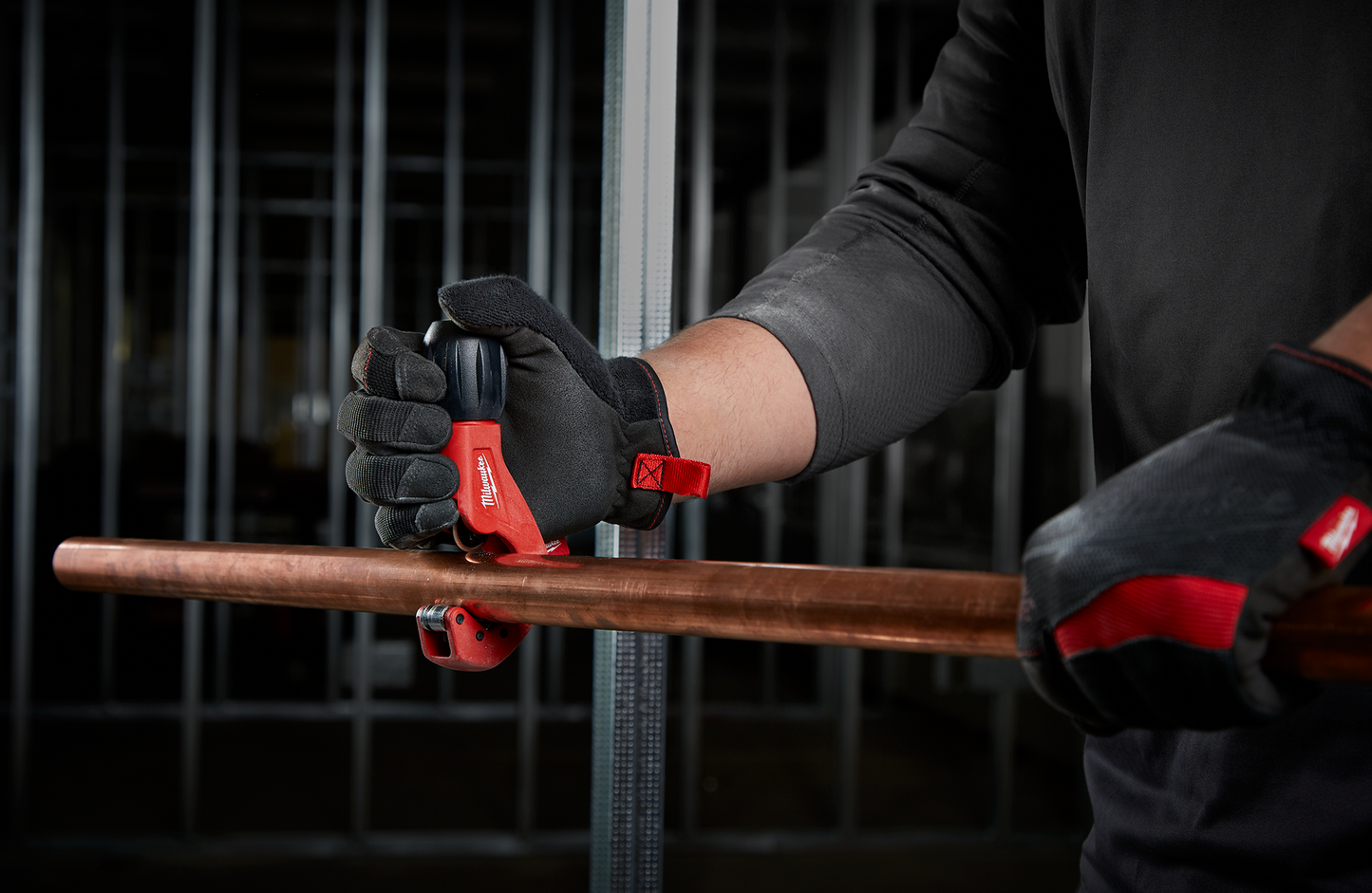 Person wearing black gloves using red compact tubing cutter on copper pipe for home improvement tasks