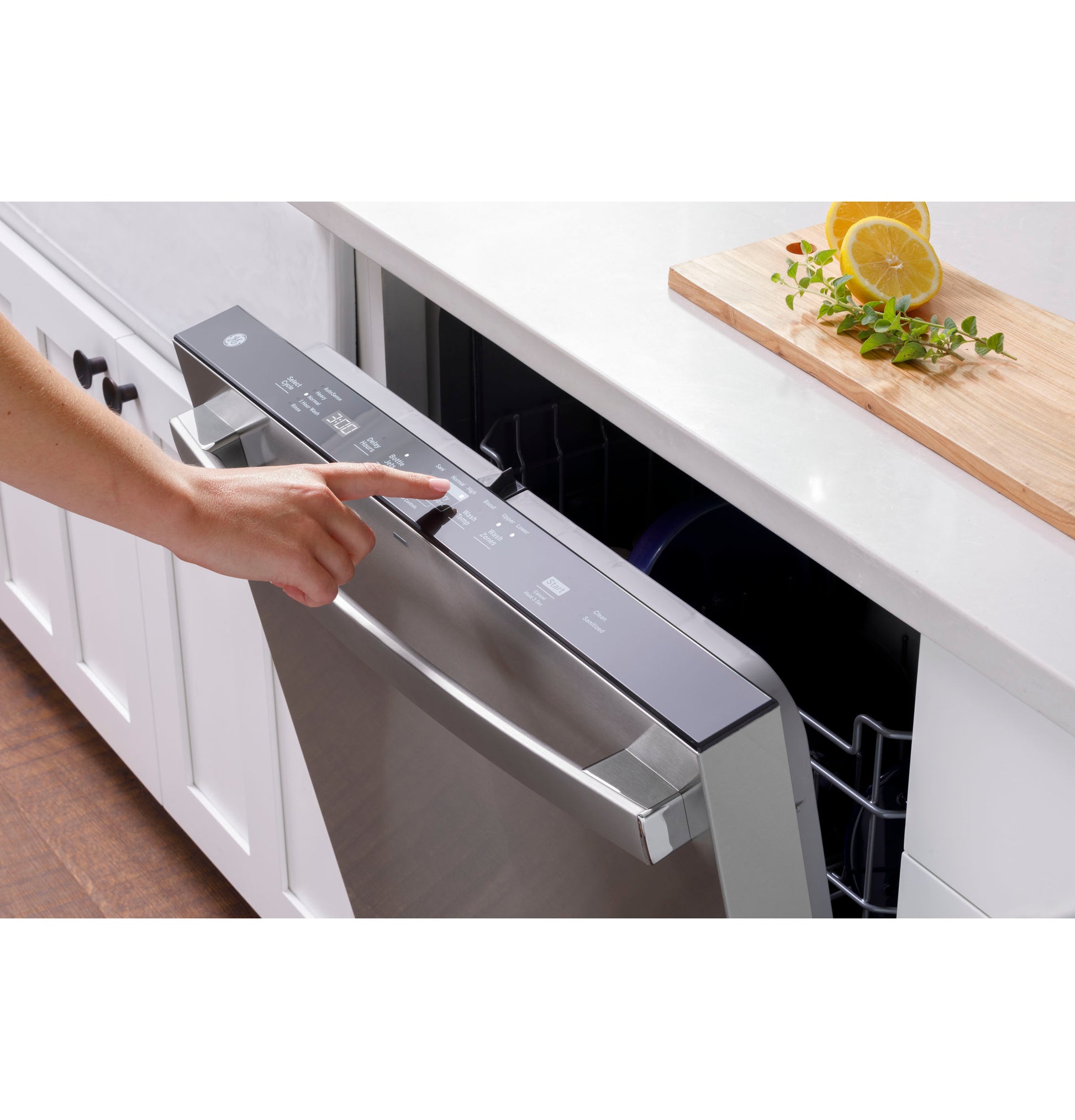 Person selecting settings on stainless steel top control dishwasher integrated into white kitchen cabinetry with cutting board nearby